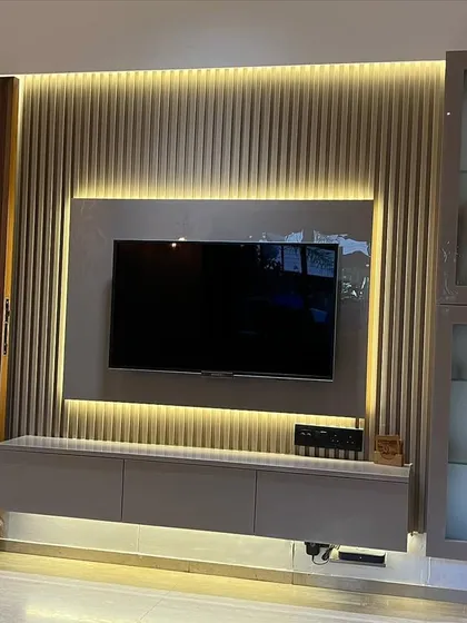 A well-designed TV unit can be the centerpiece of a living room. This floating unit features a laminate finish, a fluted panel wall with concealed backlighting, and a glass-fronted display cabinet for a clean and sophisticated entertainment area.
