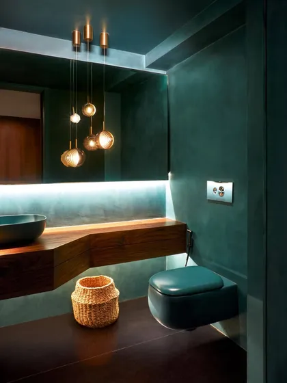 A powder room at the Baid Residence with a dramatic turquoise lime-wash finish. A floating wood counter, Bocci pendant lights, and a colored WC from Bathline Sensations create a moody, immersive experience.