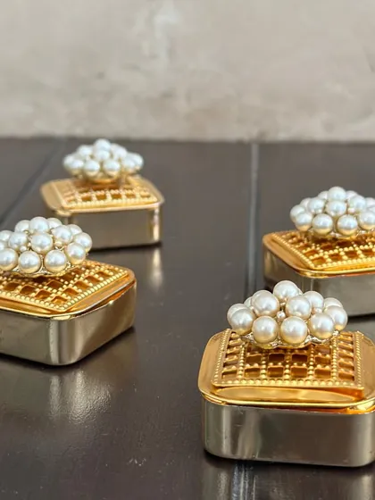 A close-up of my classic pearl-topped coin boxes. The intricate design on the golden box and the luster of the pearls make this a truly elegant shagun gift.