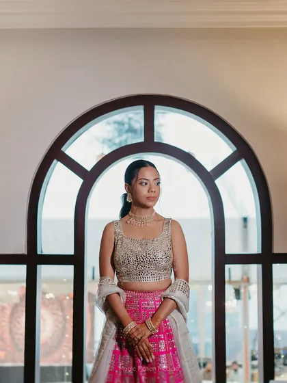 A portrait of the bride against an arched window. Her natural, skin-like makeup looks flawless in the soft light, paired with a simple ponytail for an elegant and modern Sangeet look.