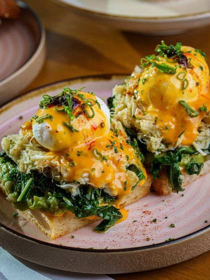 A luxurious take on Eggs Benedict, topped with crab meat and a vibrant hollandaise sauce. The close up shot highlights the rich textures and premium ingredients, perfect for an upscale brunch menu.