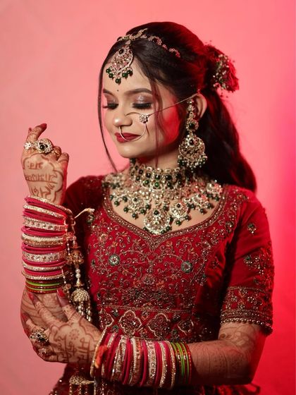 A close-up shot of a bride in a deep red velvet lehenga. Her makeup features soft smokey eyes and a red lip, perfectly complementing the rich texture of her outfit.