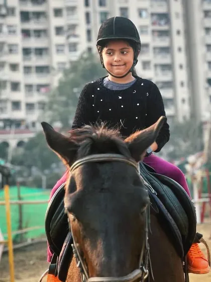 A young girl smiles for the camera from atop her horse, showcasing the joy and confidence that riding can inspire.