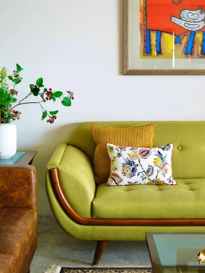 A close-up of the vibrant green sofa, styled with a mix of textured and patterned cushions. The warm wood accents and the pop of color from the artwork create a corner that is both cheerful and chic.
