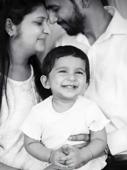 A joyful black and white family portrait, with the baby's bright smile at the center of his parents' loving gaze.