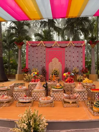 A vibrant outdoor stage under a colorful pink, yellow, and white canopy, set amongst palm trees.