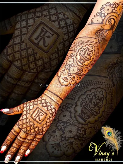 A personalized back-of-hand design featuring the initial 'K' in a square frame. The arm includes a kalash (pot) motif, symbolizing prosperity.