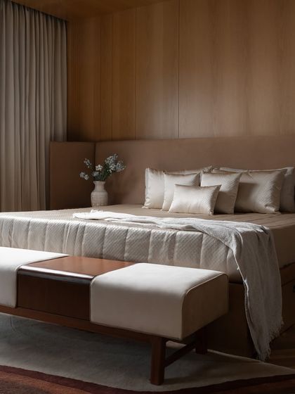A view of the custom bench at the foot of the bed, which combines dark wood with light upholstery, reflecting the room's sophisticated material palette.
