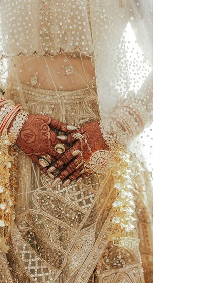 It's all about the details. This close-up shows the bride's henna-adorned hands, traditional red and white bangles, and the intricate kalire, all beautifully set against the delicate fabric of her lehenga.