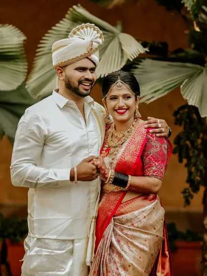 A classic portrait of a South Indian couple on their wedding day, their coordinated white and red outfits glowing with happiness.