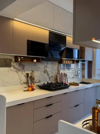 A modern L-shaped kitchen with beige handleless cabinets and a marble-patterned backsplash. This design is clean, stylish, and provides plenty of counter space for cooking.