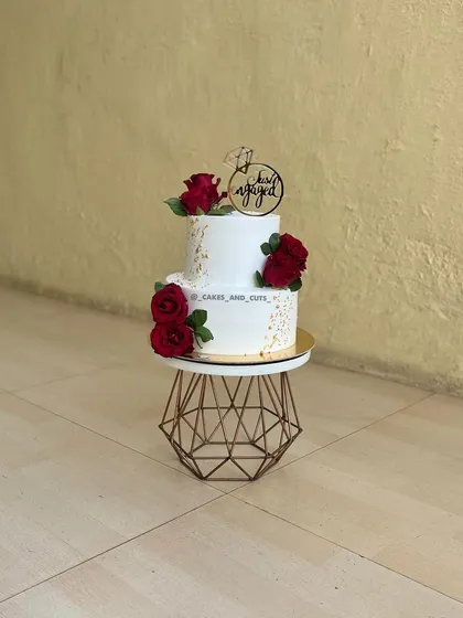 A classic two-tier engagement cake decorated with beautiful fresh red roses and gold flakes. The "Just Engaged" topper makes it a perfect centerpiece for a ring ceremony.