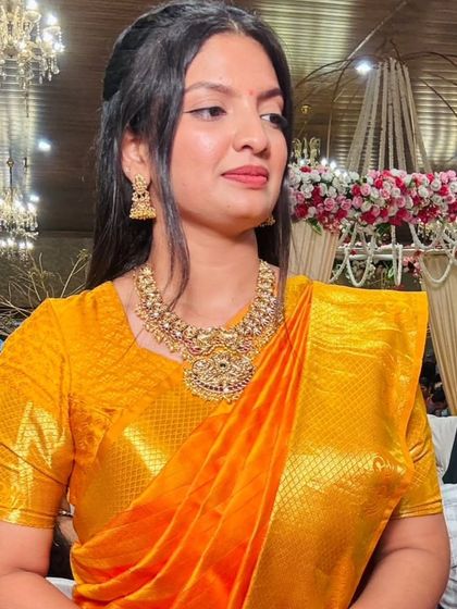 A happy client at a wedding, dressed in a vibrant yellow saree and a beautiful antique-finish temple necklace set.