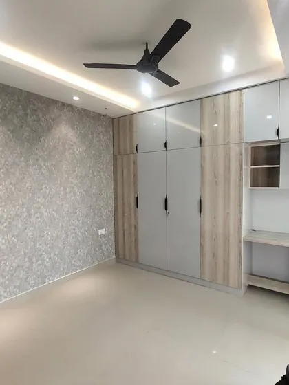 A finished bedroom with a full-wall wardrobe and an integrated study unit. The combination of grey and wood-grain laminate, along with a textured wallpaper, creates a sophisticated and functional space.