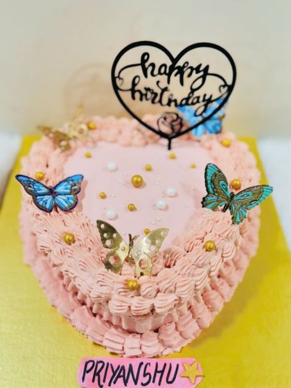 A lovely heart-shaped cake with pink frosting and decorated with delicate blue and gold butterflies.