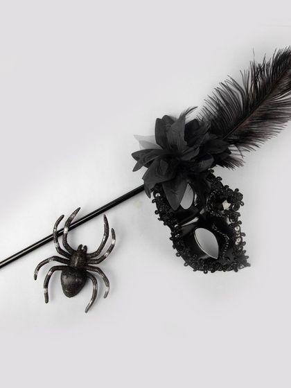A black masquerade mask on a stick, styled with a toy spider.