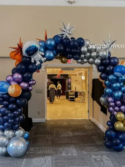 A grand entrance arch for a space-themed event. The balloon arch is made of metallic shades of blue, silver, and purple, with astronaut and star accents to welcome guests.