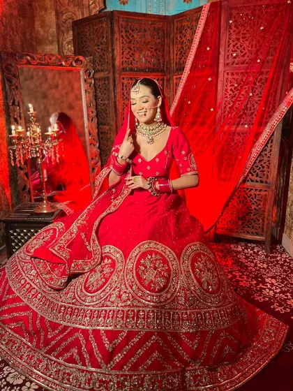 A smiling bride in a classic red lehenga. The rich color and detailed gold embroidery create a joyful and celebratory look, perfect for your wedding photos.