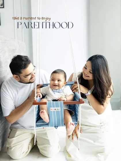 Take a moment to enjoy parenthood. A happy family gathers around their baby in a swing during a bright and airy studio session.