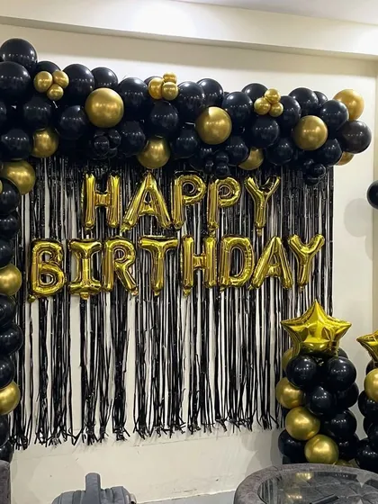 A bold and classic birthday backdrop using a black and gold balloon arch and a black shimmer curtain.