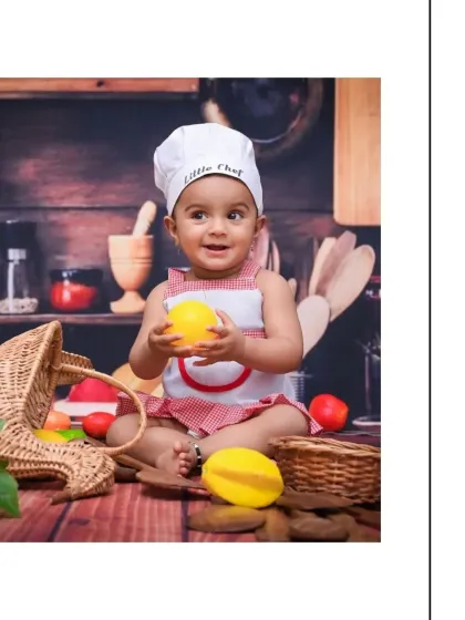 A delightful portrait of the baby chef holding a toy lemon with a sweet smile. The detailed kitchen-themed backdrop makes this creative baby photoshoot feel authentic and fun.
