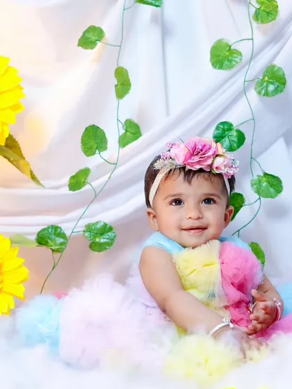 A baby girl in a pastel rainbow dress, sitting in a field of clouds and sunflowers. A dreamy and colorful setup.