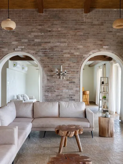 In our Alibaug villa project, 'Ekaant', we used an exposed brick wall, arched doorways, and custom log-wood tables to create an earthy, rustic feel. The design is inspired by the Indian countryside and Balinese aesthetic, focusing on natural materials and organic shapes for a tranquil getaway.