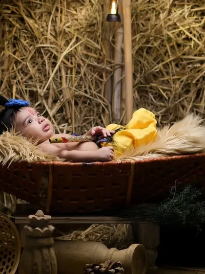 A newborn Krishna resting in a rustic basket swing, set against a backdrop of hay. This is a unique and gentle take on the Janmashtami theme for very young babies.