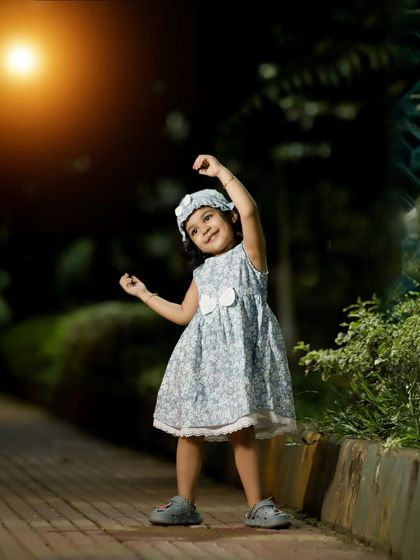 A joyful, candid shot of a little girl dancing on a pathway at dusk. The warm glow of the light adds a magical quality to this spontaneous moment of happiness.