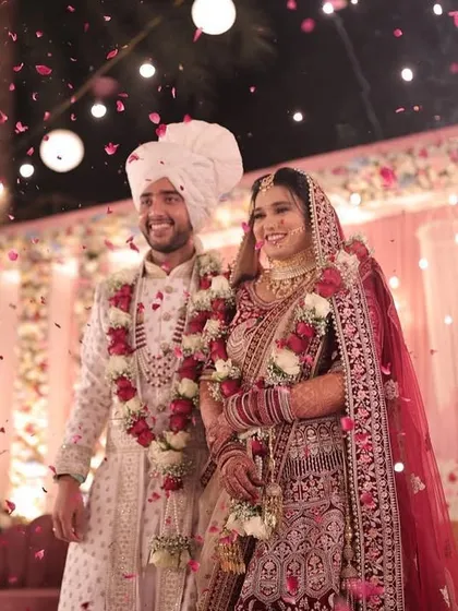 A happy couple during their varmala ceremony, showered with flower petals. The stage is decorated with a beautiful arrangement of red and white flowers, creating a classic and celebratory backdrop.