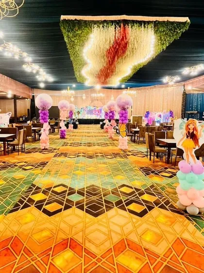 A large-scale fairy-themed birthday party in a banquet hall, with character cutouts, balloon pillars, and a stunning floral ceiling installation.