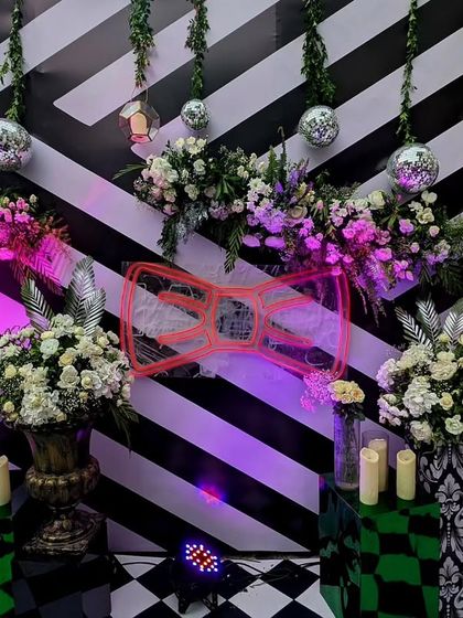 A bold and graphic photo-op area with a black and white striped backdrop. The design is accented with a neon sign, disco balls, and floral arrangements, creating a fun, retro-glam vibe.