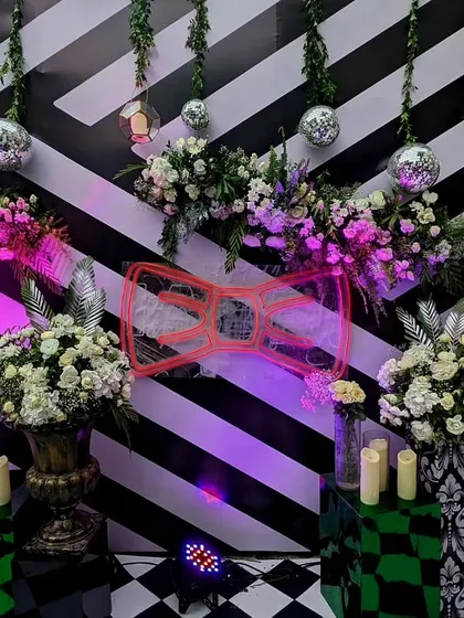 A bold and graphic photo corner for a Sangeet, with a black-and-white striped background, a quirky neon sign, and disco balls hanging from the ceiling.