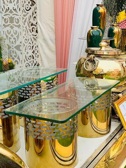 A close-up of a wedding buffet line featuring gleaming gold chafing dishes and custom decor pieces. The combination of metallic finishes and lush greenery creates a look of pure opulence.