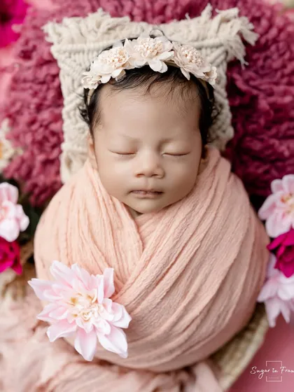 A sweet newborn in a peach-colored wrap, surrounded by pink and peach flowers.