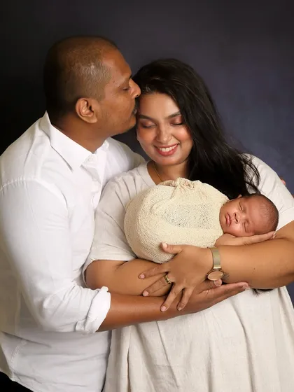 A tender moment between new parents and their baby. The father's gentle kiss on the mother's forehead shows the love and awe of this special time. This is a classic newborn family portrait.