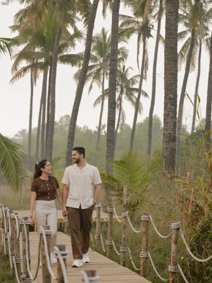 A candid shot of Vinay and Yachi walking and talking on a wooden boardwalk. Surrounded by palm trees, this image captures their easy-going chemistry and the relaxed vibe of their shoot.
