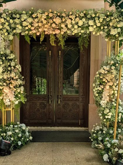 An entrance that breathes elegance. Here, I used cascading arches of white roses, baby's breath, and fresh greenery to frame the doorway, creating a soft, romantic, and timeless welcome for a garden-themed wedding ceremony.