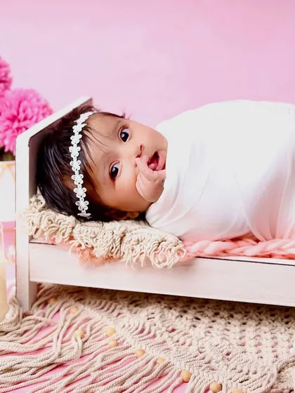 An alert and curious baby peeking out from her tiny bed. This shot captures her sweet expression and the beautiful details of the pink-themed setup.