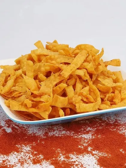 A vibrant shot of savory snack strips on a plate, with a sprinkle of red chili powder to emphasize the spicy flavor profile. This type of product photography helps customers visualize the taste and texture.