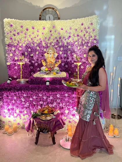 A full view of the stunning purple ombré floral mandap. The gradient effect, moving from deep purple to white, creates visual depth, while the client's presence shows how beautifully the decor complements the home environment.