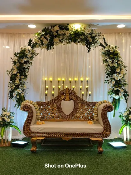 An engagement stage setup at Jakkur with a white and green theme. The floral arch is complemented by bouquets in wooden crates and a beautiful golden sofa.