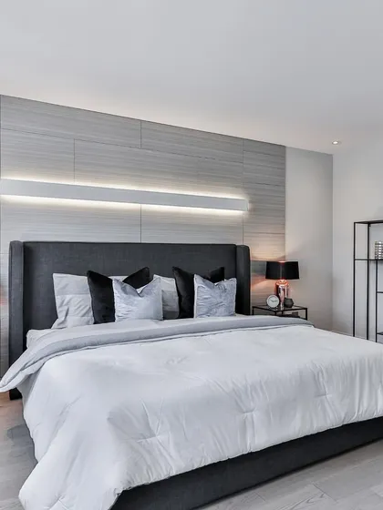 This bedroom demonstrates how a minimalist color palette of grey and white can feel incredibly luxurious. The design relies on texture, from the paneled accent wall to the soft bedding, with a sleek horizontal light fixture adding a contemporary touch.