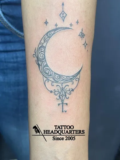 An ornamental crescent moon tattoo, rich with filigree details and sparkling stars. This design blends spiritual symbolism with decorative art.