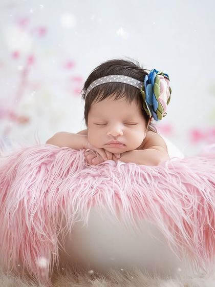 A newborn rests on a fluffy pink cushion, with a dreamy, bokeh background of pink and white, creating a soft and magical portrait.