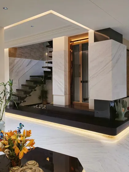 A sneak peek into a penthouse we designed, featuring a central design element that incorporates a private lift, a spiral staircase, and an indoor water body. The combination of white marble, dark wood, and strategic under-lighting creates a striking focal point.