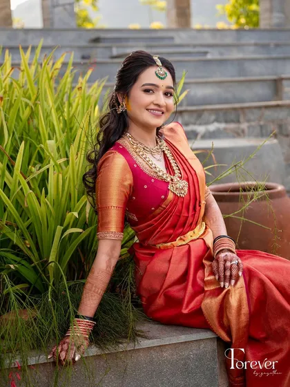 A bride sitting gracefully in her red Kanchipuram saree. The simplicity of her custom blouse allows the rich color of the saree and her antique jewelry to stand out.