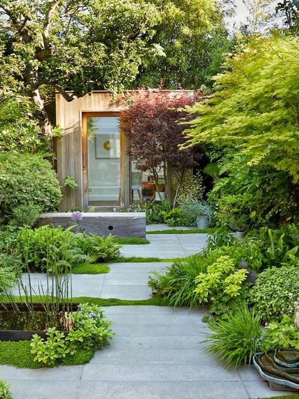 A small garden studio is seamlessly integrated into the landscape. The path, lined with lush plants and a small pond, leads to a quiet retreat, showing how we can design functional outbuildings within a garden setting.