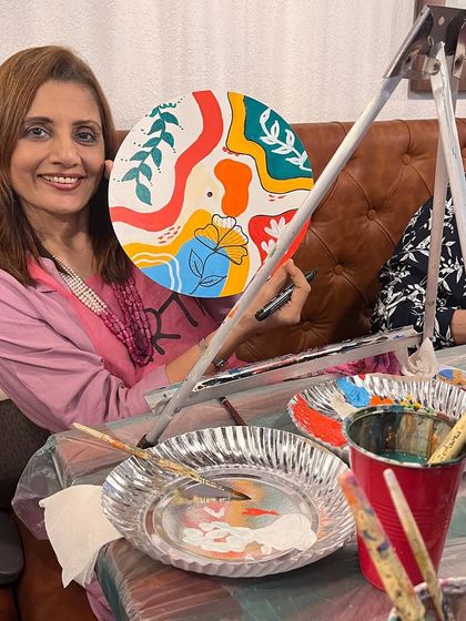 A guest at a kitty party holding up her finished boho clock. Everyone leaves with a unique, hand painted piece of home decor.