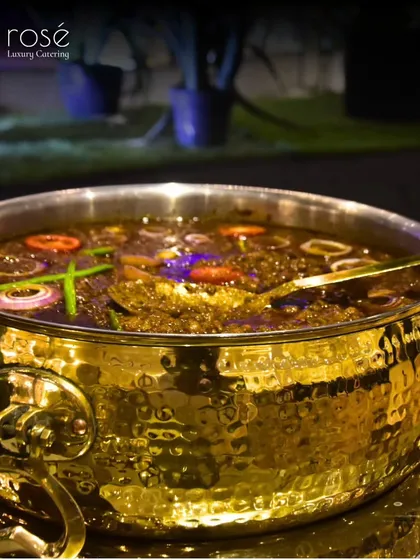 A close-up of a rich, dark curry in a hammered brass pot. This image highlights the deep flavors and luxurious presentation that are the hallmarks of our service.